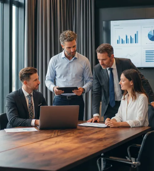 Quatre collègues en réunion analysent des données sur un ordinateur et une tablette.