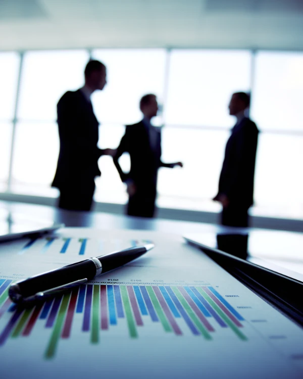 Silhouettes de trois professionnels discutant devant un graphique et un stylo au premier plan.