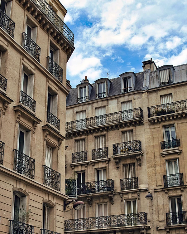Façades d'immeubles haussmanniens avec balcons en fer forgé sous un ciel bleu nuageux.