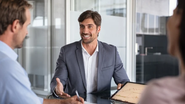 Un homme d'affaires souriant en costume gris présente des graphiques sur tablette en réunion.