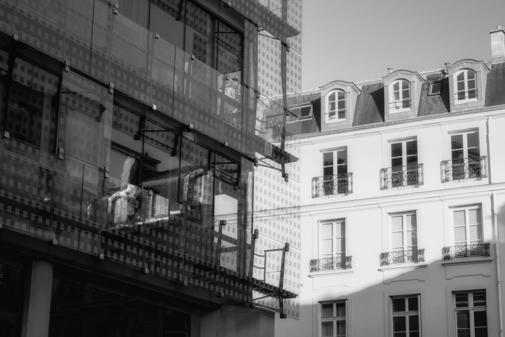 Image en noir et blanc juxtaposant un immeuble moderne vitré et un bâtiment classique traditionnel.