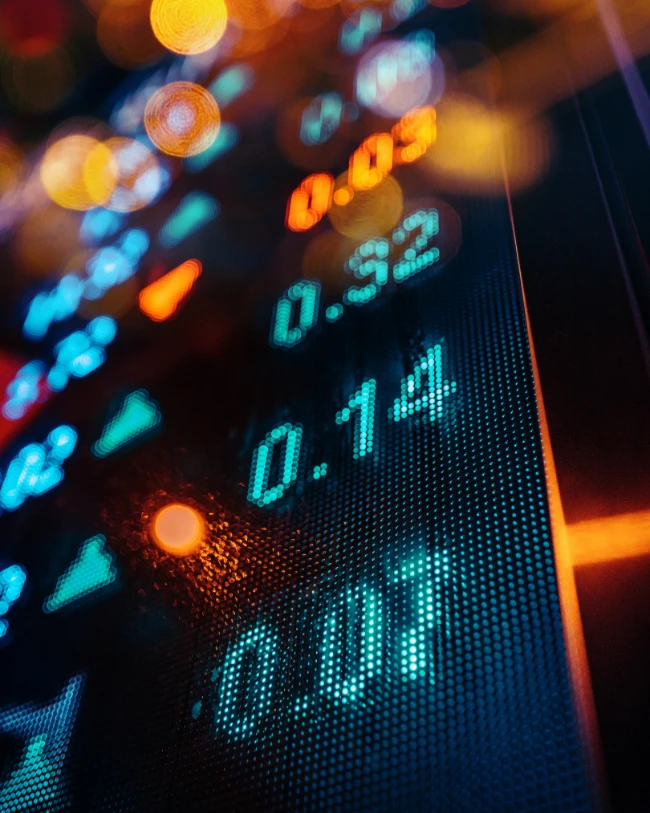 Gros plan sur un écran boursier affichant des chiffres lumineux avec un effet de flou bokeh.